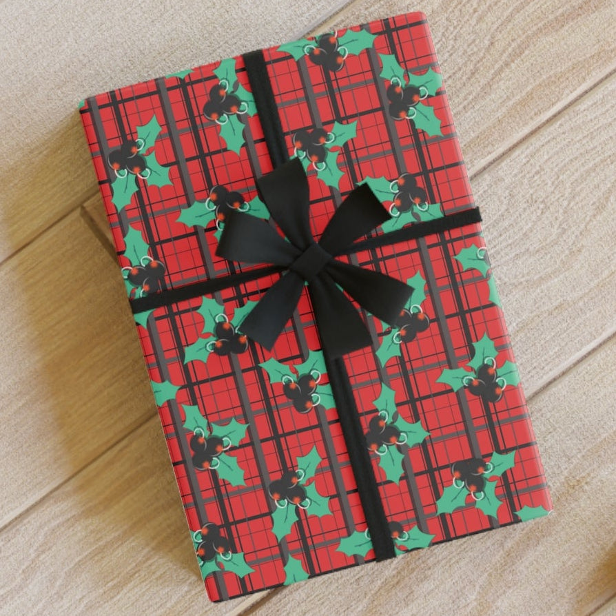 Red and green plaid gift box with black ribbon on a wooden floor.