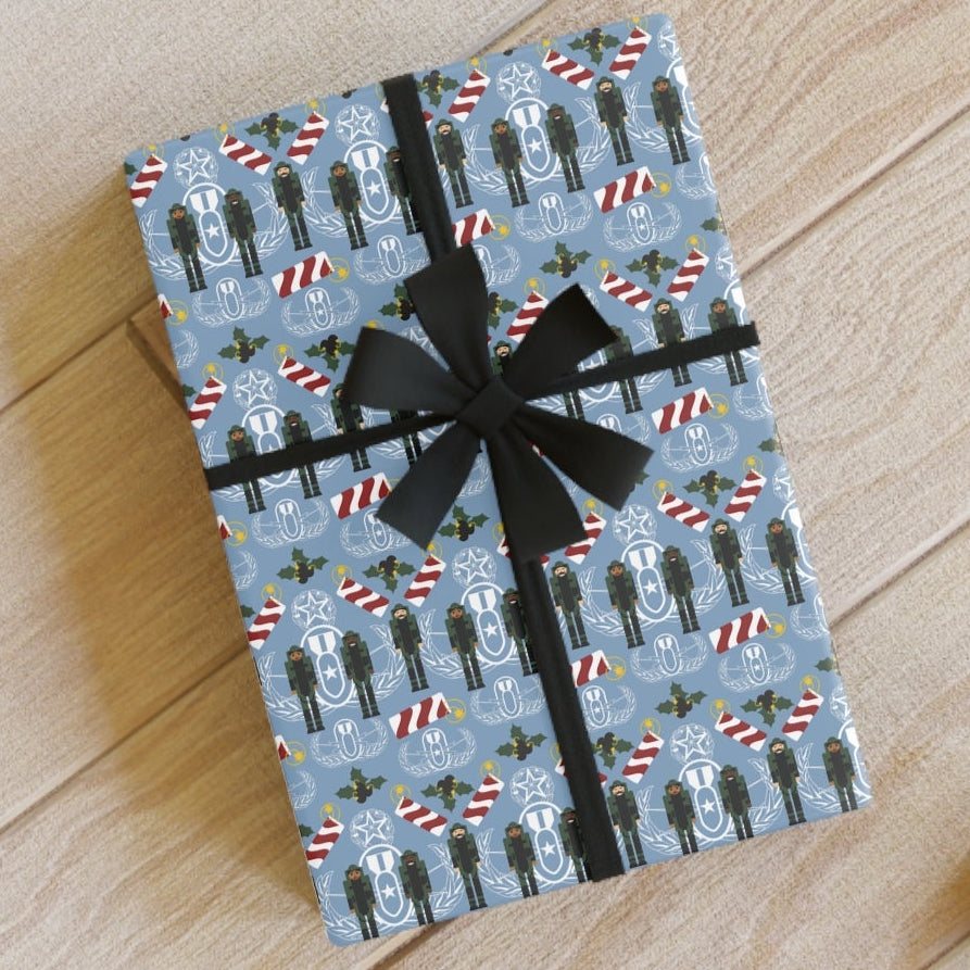 Gift box with blue pattern and black ribbon on a wooden surface with scissors and tape.