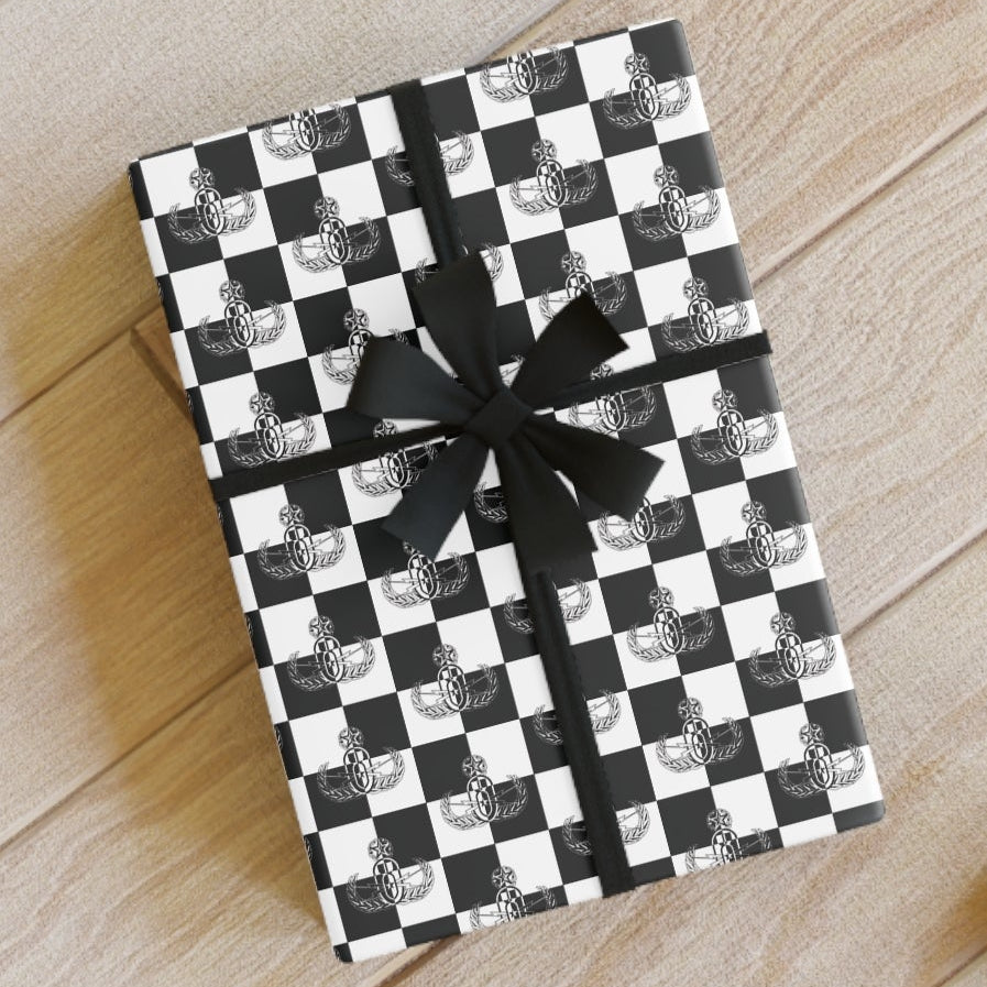 Checkered gift box with a bow on a wooden floor, surrounded by ribbons and scissors.
