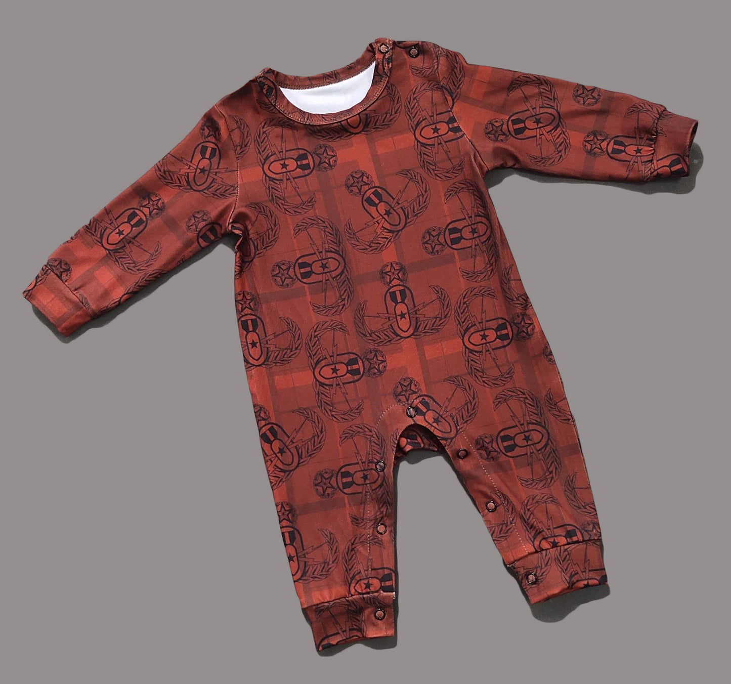 A flat lay of a long sleeve red and black EOD Badge Plaid onesie with snap closure on leg inseam on a solid grey background